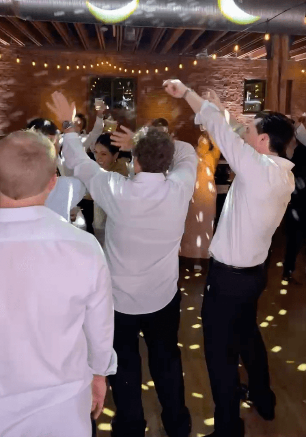 Wedding guests raising their hands and dancing under string lights.