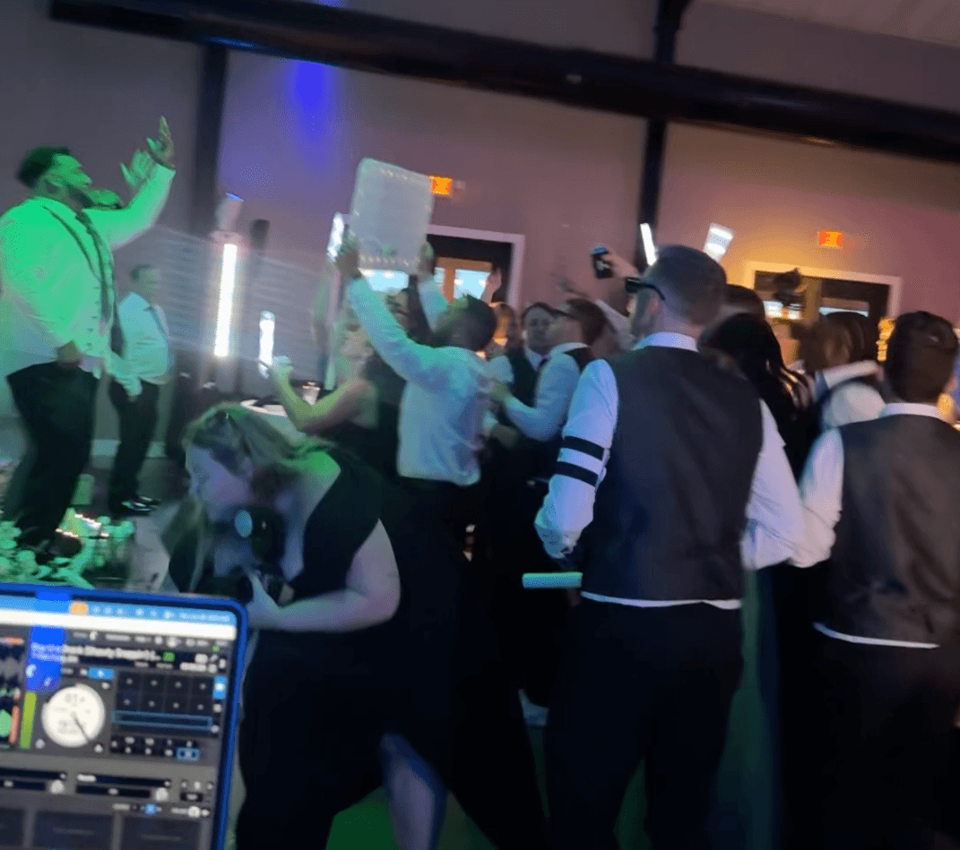 Guests celebrating on a packed dance floor beside the DJ booth.