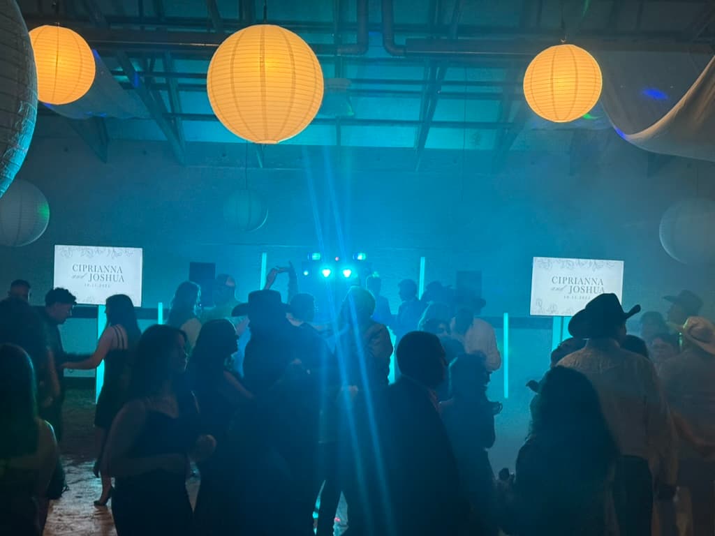 Guests celebrating on a dance floor under blue lighting beams and warm hanging lanterns.